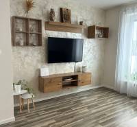 Praktický 3-izbový byt v súkromnej ulici v Šamoríne - Obývačka v 3-izbovom byte s podlahou s dreveným dekorom, zavesenou TV a dekoráciami.