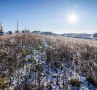 Stavebný pozemok v lokalite Medzi Vodami - Zasnežený pozemok v Mlynici s obydliami na pozadí, ideálny pre bývanie.