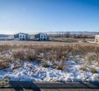 Stavebný pozemok v lokalite Medzi Vodami - Zasnežené pozemky na bývanie v Mlynici so slnečným počasím a viditeľnými domami v pozadí.