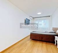 Predaj, dvojizbový byt Bratislava Ružinov, Trnavská ... - Spálňa v 2-izbovom byte s posteľou, nočným stolíkom a televízorom, má podlahu s dreveným dekorom.