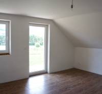 Na predaj – veľkorysý rodinný dom s úžasným výhľadom a pozemkom - Svetlá izba s oknami, podlaha s dreveným dekorom a presklenými dverami v rodinnom dome.