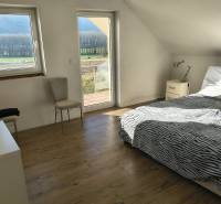 Na predaj – veľkorysý rodinný dom s úžasným výhľadom a pozemkom - Svetlá spálňa v rodinnom dome s posteľou, stoličkou a podlahou s dreveným dekorom.