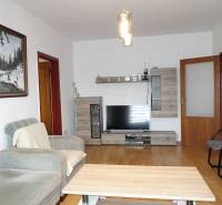 PREDAJ- 3-iz. byt, Homolova - Dúbravka, 67 m2, 11./12. posch., lodžia - Obývačka 3-izbového bytu s pohodlnou pohovkou, nábytok s dreveným dekorom a televízorom.