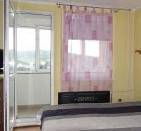 PREDAJ- 3-iz. byt, Homolova - Dúbravka, 67 m2, 11./12. posch., lodžia - Spálňa so vstupom na balkón v 3-izbovom byte s fialovými závesmi na okne.