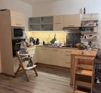 Na predaj moderný 4-izbový byt s veľkou terasou a súkromnou záhradou - Kuchyňa v 4-izbovom byte s podlahou s dreveným dekorom, detskou stoličkou a hračkami.