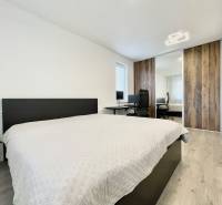 Na predaj štýlový 2-izbový byt s loggiou a parkovaním – TN, Na Pažiti - Dvojposteľ v 2-izbovom byte, šatník so zrkadlom a pracovný kút na drevenom dekore.