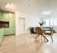 Na predaj štýlový 2-izbový byt s loggiou a parkovaním – TN, Na Pažiti - Obývačka v 2-izbovom byte s podlahou s dreveným dekorom a zelenou kuchyňou.