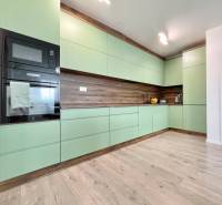 Na predaj štýlový 2-izbový byt s loggiou a parkovaním – TN, Na Pažiti - Kuchyňa v 2-izbovom byte s mätovo zelenými skrinkami a podlahou s dreveným dekorom.