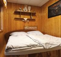 Predaj, chata Byšta - EXKLUZÍVNE HALO REALITY - Spálňa na chate s drevenou stenou a policami nad posteľou.