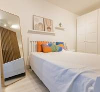 Slnečný 1,5i byt s loggiou a parkovaním - Spálňa v 1-izbovom byte s posteľou, farebnými vankúšmi, zrkadlom a veľkou skriňou.