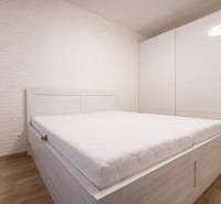 Zariadený 2i byt s lodžiou v rezidencii Pri Mýte - Svetlá spálňa s bielou posteľou, vstavaná skriňa, podlaha s dreveným dekorom v 2-izbovom byte.