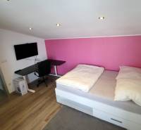 NADŠTANDARDNÝ 5 izbový dom Jánošíkova / Piešťany - Izba v rodinnom dome s podlahou s dreveným dekorom, posteľou a čiernym stolom.