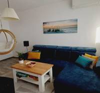 Na predaj 3izbový byt Tranovského , Dúbravka - Obývacia izba s modrou sedačkou, hojdačkou, knihovnicou a podlahou s dreveným dekorom.