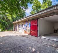 Pozrite si 17m², ZREKONŠTRUOVANÚ garáž, pri nemocnici Kramáre - Garáže s graffiti a otvorenými dverami na ulici Opavská obklopené zeleňou.