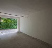 Pozrite si 17m², ZREKONŠTRUOVANÚ garáž, pri nemocnici Kramáre - Prázdna garáž na ulici Opavská, s výhľadom na zeleň a betónovou podlahou.