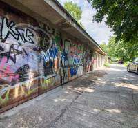 Pozrite si 17m², ZREKONŠTRUOVANÚ garáž, pri nemocnici Kramáre - Graffiti pokrývajú garáže na ulici Opavská, autá parkujú na ceste obklopenej stromami.