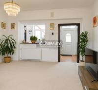 Predaj, rodinný dom Beša - Obývacia izba v rodinnom dome s bielymi stenami, kvetinami a televízorom na stolíku.