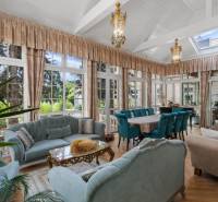 Exkluzívna honosná kúria | 3 ha pozemok | Dunakiliti - HU - Priestranný svetlý interiér s presklenými stenami, dekoratívnymi lustrami, modrými sedačkami a podlahou s dreveným dekorom.