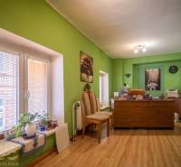 Exkluzívne: Predaj budovy v centre mesta Poprad - Kancelária s dreveným dekorom podlahy, zelené steny, pracovný stôl a dekorácie.