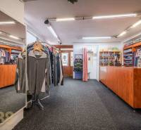 Exkluzívne: Predaj budovy v centre mesta Poprad - Obchod s odevmi s kobercom, dreveným pultom a veľkým zrkadlom.