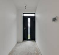 Novostavba samostatne stojaceho RD v štandarde, nízka spotreba - Biely interiér Rodinného domu s tmavými vstupnými dverami a drsnou podlahou s dreveným dekorom.