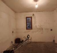 Rodinný dom v obci Čebovce v okrese Veľký Krtíš. - Suterén s oknom v rodinnom dome, steny s prasklinami a jednoduchým osvetlením.