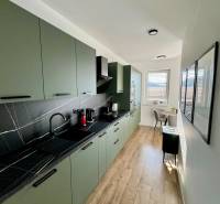 PREDAJ - 2-izbový byt v nádhernej lokalite Dvorníky - Kuchyňa v 2-izbovom byte s podlahou s dreveným dekorom a zelenými skrinkami.