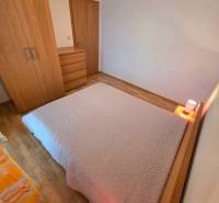 Apartmán, Nová Lesná, 46m2 + balkón, park. miesto, zariadený  - Spálňa v rekreačnom apartmáne s posteľou a nábytkom na podlahe s dreveným dekorom.