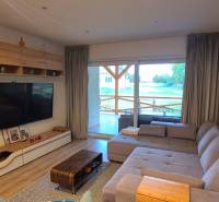 Na predaj 4 izbový RD v obci  Studienka, garáž, sauna, pozemok 719 m2 - Obývačka rodinného domu s pohovkou, veľkým televízorom a podlahou s dreveným dekorom.