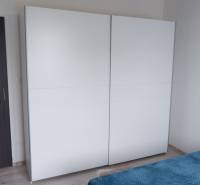 Ponúkame na predaj 3 izbový radový dom v obci Rastislavice. - Biela skriňa a posteľ s modrou prikrývkou v interiéri rodinného domu.