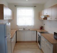 Ponúkame na predaj 3 izbový radový dom v obci Rastislavice. - Kuchyňa v rodinnom dome s bielymi skrinkami a podlahou s dreveným dekorom.