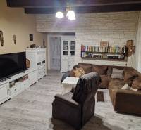 Krásny rodinný dom s rozľahlým pozemkom - Obývacia izba s rohovou sedačkou, bielym nábytkom a podlahou s dreveným dekorom v rodinnom dome.