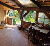 Krásny rodinný dom s rozľahlým pozemkom - Rustikálna terasa rodinného domu s dreveným nábytkom a výhľadom na záhradu.