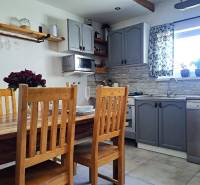 Exkluzívne na predaj 5 izbový rodinný dom - Kuchyňa v rodinnom dome s dreveným stolom, stoličkami a sivými skrinkami.