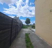 Exkluzívne na predaj 5 izbový rodinný dom - Rodinný dom vo Veľkej Mači vedľa dreveného plota, betónová cesta, oblaky a strom.