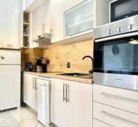 Trogir, Čiovo – pekný, zariadený apartmán len 150m od pláže - Kuchyňa v Rekreačnom apartmáne s bielym nábytkom a dreveným dekorom na stene.