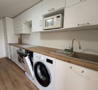 NA PRENÁJOM krásny 1 izbový apartmán so záhradou v srdci Komárna - Kuchyňa v 1-izbovom byte s bielou linkou, práčkou a podlahou s dreveným dekorom.