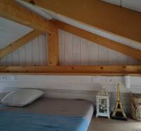 Tiny house - malý domček - Podkrovná spálňa v rodinnom dome s dreveným stropom a dekoráciami vedľa postele.