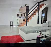 Prenájom ubytovacieho zariadenia – Šaľa Veča s kapacitou 50 osôb - Obývacia izba s kuchynským kútom, schodiskom, gaučom, skleneným stolíkom a podlahou s dreveným dekorom.