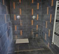 Prenájom ubytovacieho zariadenia – Šaľa Veča s kapacitou 50 osôb - Kúpeľňa s tmavými obkladmi, sprchou a bielym radiátorom v budove.