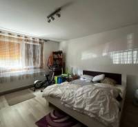 Rodinný dom s prístavbou na  podnikanie – Tešedíkovo - Spálňa s posteľou, cvičebnými strojmi, knihovničkou a podlahou s dreveným dekorom v rodinnom dome.