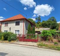 Výborný rodinný dom pre pohodlné bývanie - Rodinný dom v Tachtoch, s červenou strechou, plotom a záhradou v zelenom prostredí.