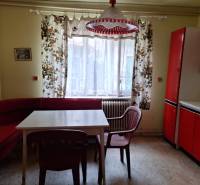 Výborný rodinný dom pre pohodlné bývanie - Kuchyňa v rodinnom dome s červeným nábytkom, farebnými závesmi a plastovými stoličkami.