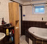 Investujte do budúcnosti - Kúpeľňa s rohovou vaňou, bielym umývadlom a dreveným nábytkom v rodinnom dome.