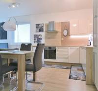 ANTOLSKÁ, 2-i byt, 54 m2 – novostavba REZIDENCIA DRAŽDIAK, zariadený - Moderná kuchyňa s jedálenským stolom, bielymi skrinkami a podlahou s dreveným dekorom v 2-izbovom byte.