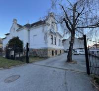 PREŠOV-ŠIRŠIE CENTRUM,POLYFUNKČNÁ BUDOVA,VL.PARKOVISKO,UL.VAJANSKÉHO - Budova na Vajanského ulici v Prešove so stromom a zaparkovanými autami.