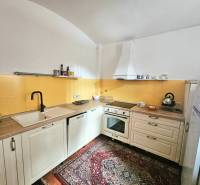  Veľkometrážny 3 izbový byt v kúpeľnom meste Trenčianske Teplice  - Kuchyňa v 3-izbovom byte s krémovými skrinkami, žltým obkladom a vzorovaným kobercom.