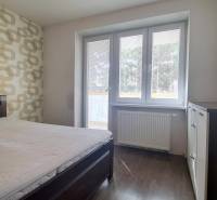 Moderný 2i byt, balkón, tehla, tichá lokalita, Kadnárova ul., Rača - Spálňa v 2-izbovom byte s posteľou, vzorovanou tapetou a podlahou s dreveným dekorom.