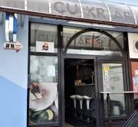 Kaviareň v Top lokalite mesta Šaľa na predaj - Obchodné priestory v Šali s veľkým oknom, dreveným dekorom a bielymi stoličkami.