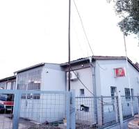 Prevádzková budova-AUTOSERVIS na predaj vo Veľkých Úľanoch - Výrobné priestory v meste Veľké Úľany so šedou fasádou a červeným autom za plotom.